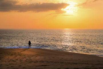 Woman stands on the ocean and looks at the sunset.