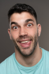 Handsome caucasian white male with black short hair and stubble with light blue t shirt looking goofy