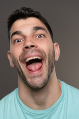 Handsome caucasian white male with black short hair and stubble with light blue t shirt looking goofy