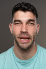 Obraz premium Handsome caucasian white male with black short hair and stubble with light blue t shirt funny face