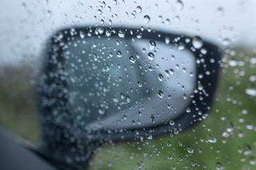 Raindrops on the car window and side mirror in the background