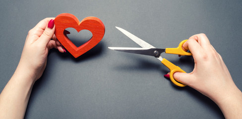 Girl cuts the red heart with scissors. The concept of breaking relations, quarrels and divorce. Betrayal of the othere. Loss of feelings for your loved one