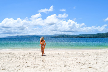 Fototapeta na wymiar young lady walking in bikini on the beach to the ocean, idyllic island with white beach and turquoise ocean
