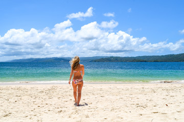 Fototapeta na wymiar Woman walking in bikini on the beach to the ocean, idyllic island with white beach and turquoise ocean