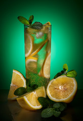 Cocktail with lemon, fresh mint and ice. Nearby are the fruits of lemon and mint. - 246184944