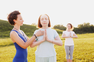 Mother and two young daughters do yoga oh in the park on a sunny summer day. Concept of health and longevity at any age