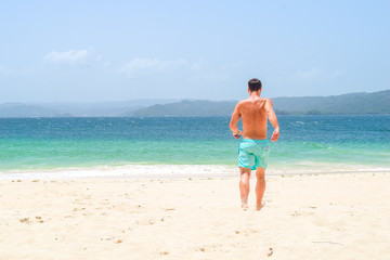 Fototapeta na wymiar Man running barefoot on the beach into the turquoise ocean on an island, caribbean sea