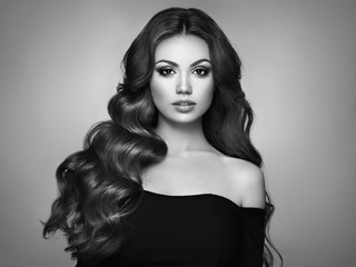 Fototapeta premium Brunette Girl with Long Healthy and Shiny Curly Hair. Care and Beauty. Beautiful Model Woman with Wavy Hairstyle. Make-Up and Black Dress