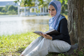 Obraz premium Happy Asian woman reading book under the tree lakeside.