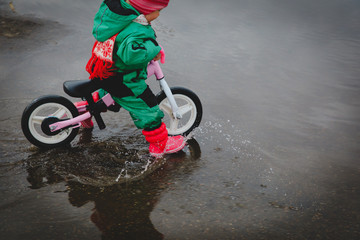 little girl riding bike in spring water puddle
