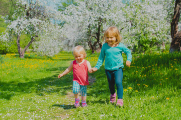 happy girls play run in spring nature, apple blossom, seasonal activities
