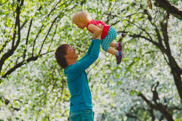happy father and little daughter play in spring nature, apple blossom