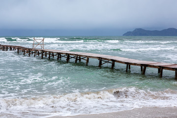 Steg am Strand wird von grün blauen Wellen umspült, copy space unten