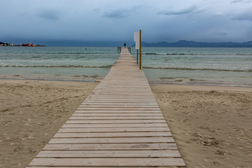 Heller Holzsteg führt über den Sandstrand ins wellige Meer hinaus, copy space