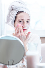 Beautiful happy woman applying cream on face moisturizing the skin. Hygiene and care for the skin at home