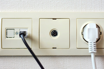 Electrical sockets on the wall with black connection internet plug and white wire. Socket set with usb cord and electricity cable with selective focus on neutral background. 
