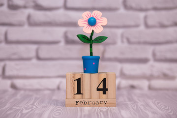 February 14. Day 14 of month on wooden calendar with toy flower on white brick background. Happy Valentines day. Love concept.