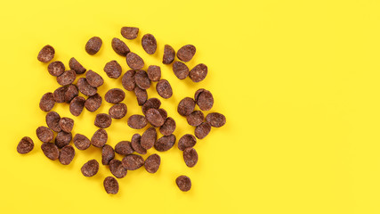 Top down view, scattered chocolate cornflake on yellow board, space for text on the right.