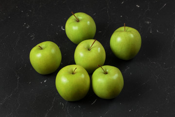 Six green / yellow apples on black marble board.