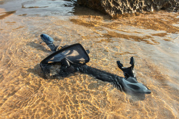 Black snorkelling tube and diving mask / goggles on sand in shallow sea water.