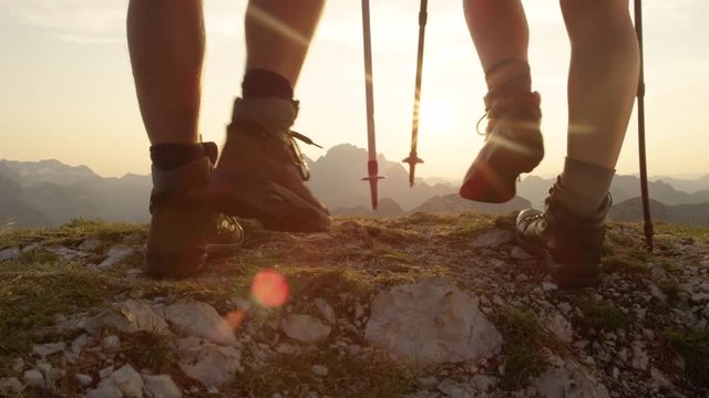 SLOW MOTION, LENS FLARE, CLOSE UP: Unrecognizable active tourists walk up the mountain peak at sunrise. Young couple wearing leather hiking boots reaches the stunning mountaintop at golden sunset.