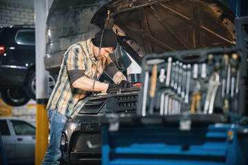 Car service. Mechanic man standing by the car with open hood and working with a tool. Tool case on the foreground