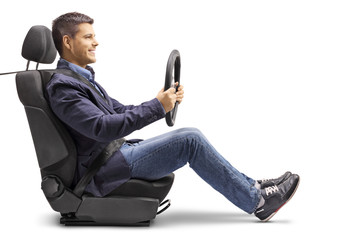 |Young man in a car seat with a fastened seat belt holding a streering wheel