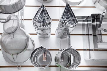 Set of metal kitchen utensils hanging on rack. Kitchen utensils hang on the shelf. Kitchen utensils hanging with steel hooks, white wall on background