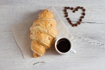 cup of coffee and croissant and heart shaped coffee beans