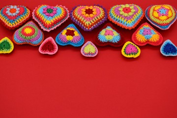 Knitted hearts of colored yarn on a red background. Valentine's Day, love, handmade, amigurumi, hobby, decoration, postcard, creative.