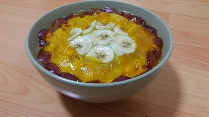 Creamy tasty sweet custard with banana pieces on surface inbowl on wooden floor