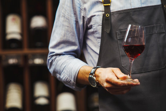 Male sommelier holds bokal with red wine in hand