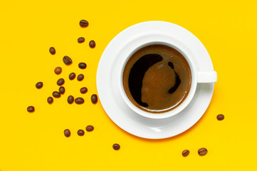 Flat lay cup of black coffee and coffee beans on yellow background top view copy space. Minimalistic food concept, morning breakfast, time to work, hot drink, coffee background
