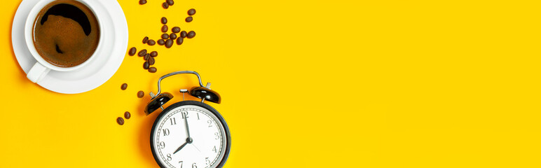 Flat lay cup of black coffee, coffee beans, black alarm clock on yellow background top view copy...