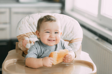 baby in the kitchen in the high chair there is a piece of bread