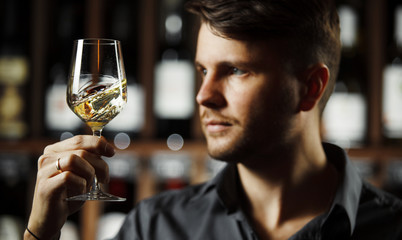 Bokal of white wine on background, male sommelier appreciating drink