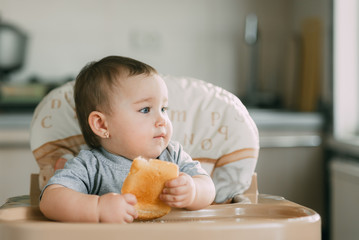 baby in the kitchen in the high chair there is a piece of bread