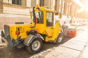 Yellow urban sweeper cleans road embankment dirt with a round brush.