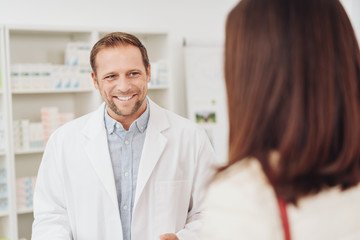 Male pharmacist smiling as he attends to a woman