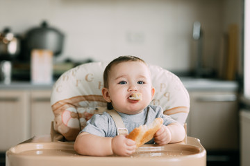 baby in the kitchen in the high chair there is a piece of bread