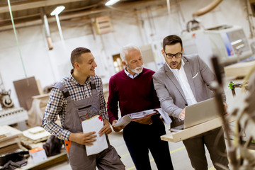 Three men standing and discuss in furniture factory