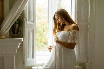 Young pregnant woman standing by the window