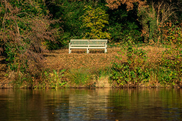 alte hölzerne Parkbank im herbstlichen Sonnenschein an einem Seeufer