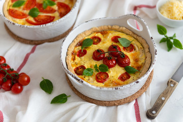 Tomato pies with basil leaves, chicken ans cheese on white tablecloth. Homemade french quiche