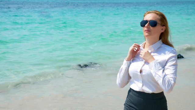Business woman in sunglasses on the beach. she rejoices in the sea and the sun. she unbuttoned her shirt and breathes in the sea air
