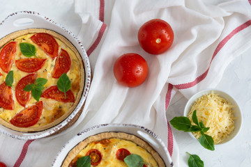 Tomato pies with basil leaves, chicken ans cheese on white tablecloth. Homemade french quiche. Top view