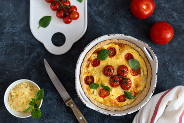 Tomato pies with basil leaves, chicken ans cheese with ingredients on dark background. Homemade french quiche. Top view