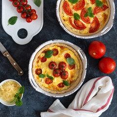 Tomato pies with basil leaves, chicken ans cheese with ingredients on dark background. Homemade french quiche. Top view