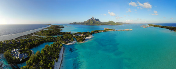 Aerial panoramic landscape view of the island of Bora Bora in French Polynesia with the Mont Otemanu mountain surrounded by a turquoise lagoon, motu atolls, re