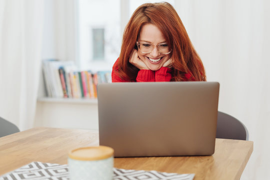 Happy young woman reading her laptop at home